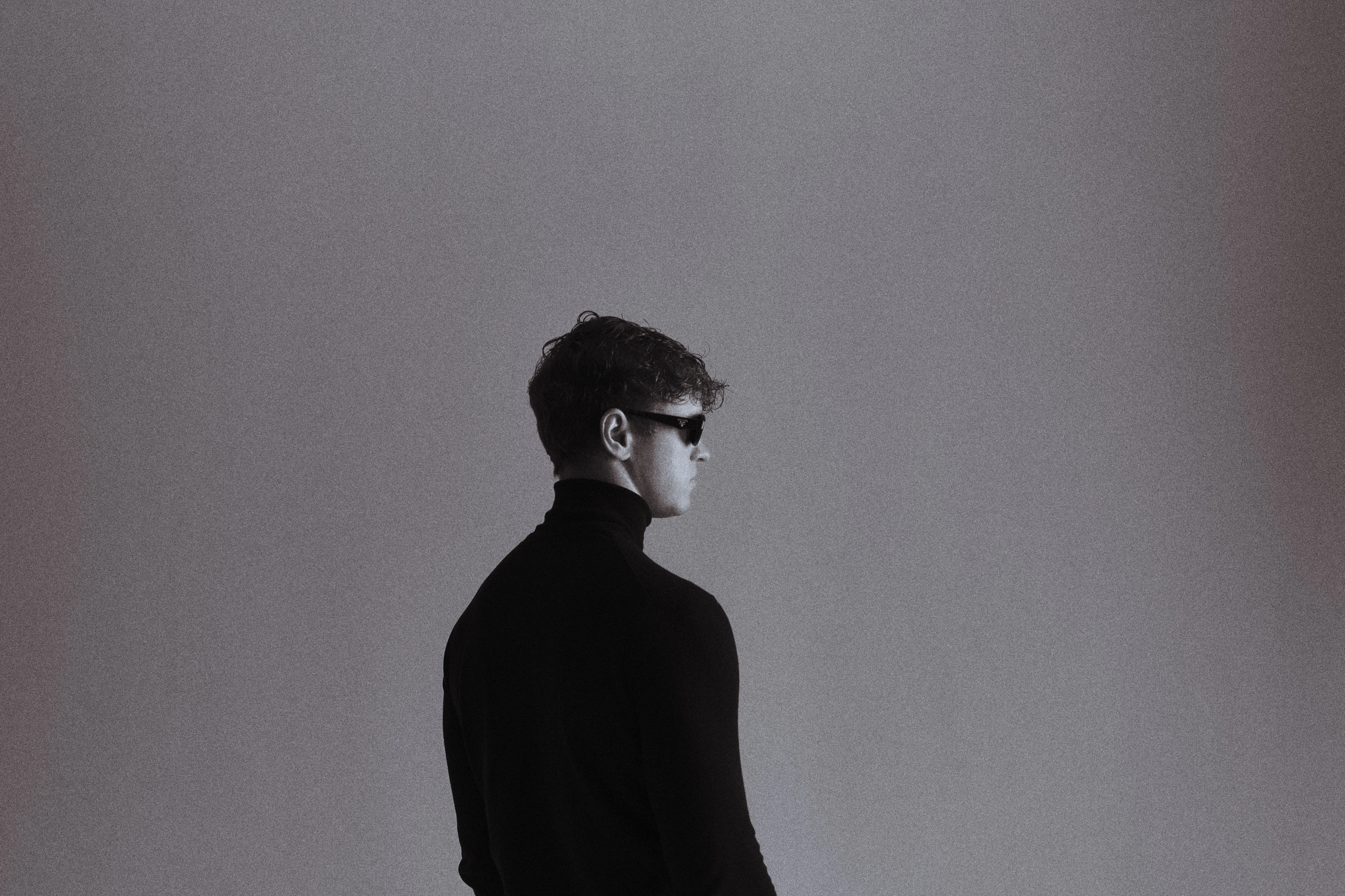 Black and white side profile in turtleneck and sunglasses against minimal grey backdrop