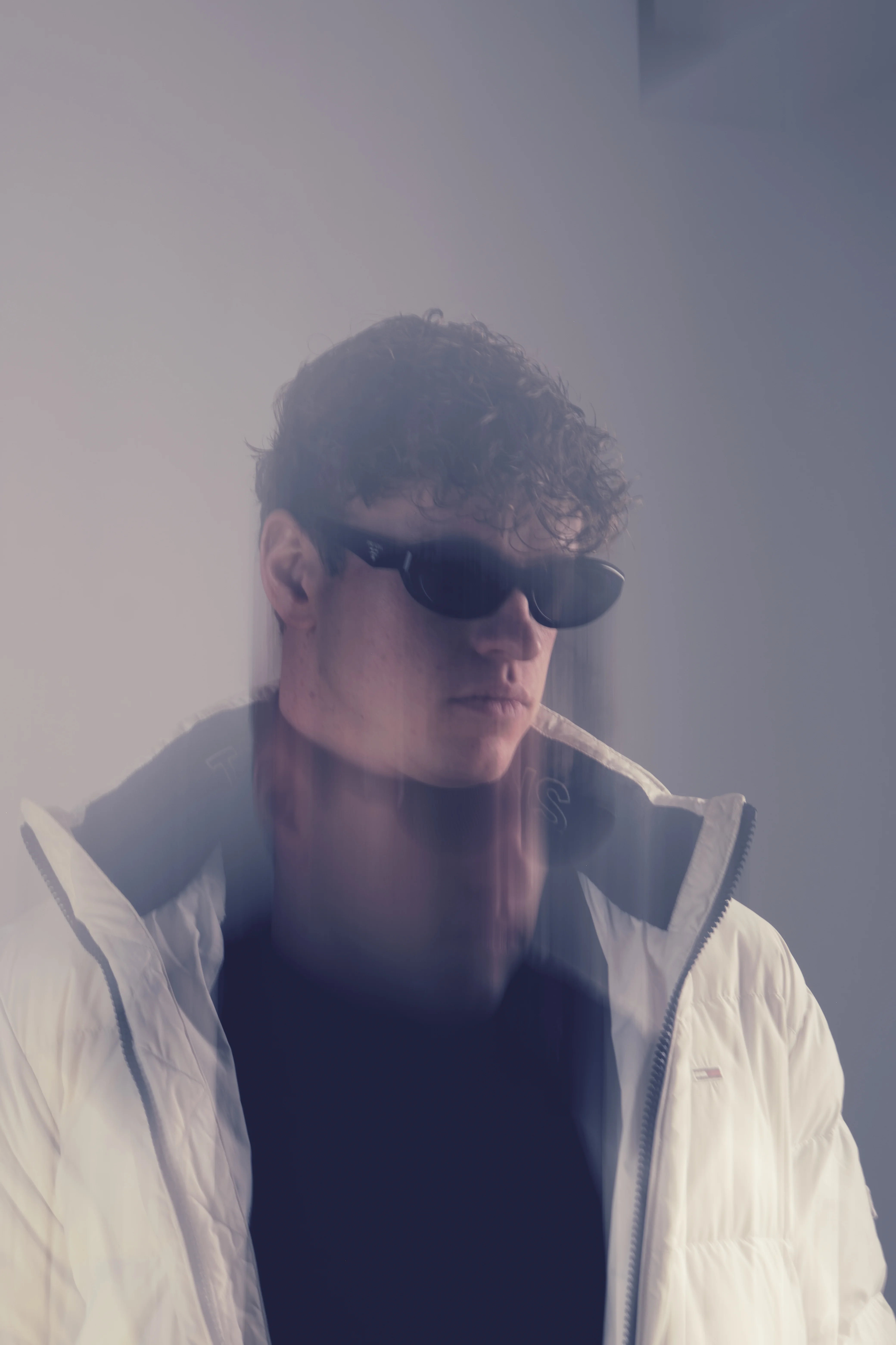 Hazy portrait with light flare in white puffer jacket, curly hair and sunglasses