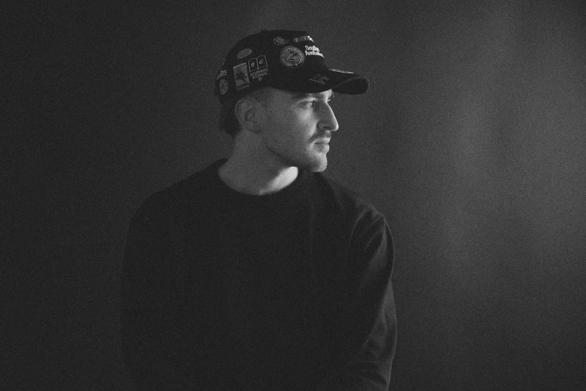 Black and white portrait looking to the side with cap and dark backdrop