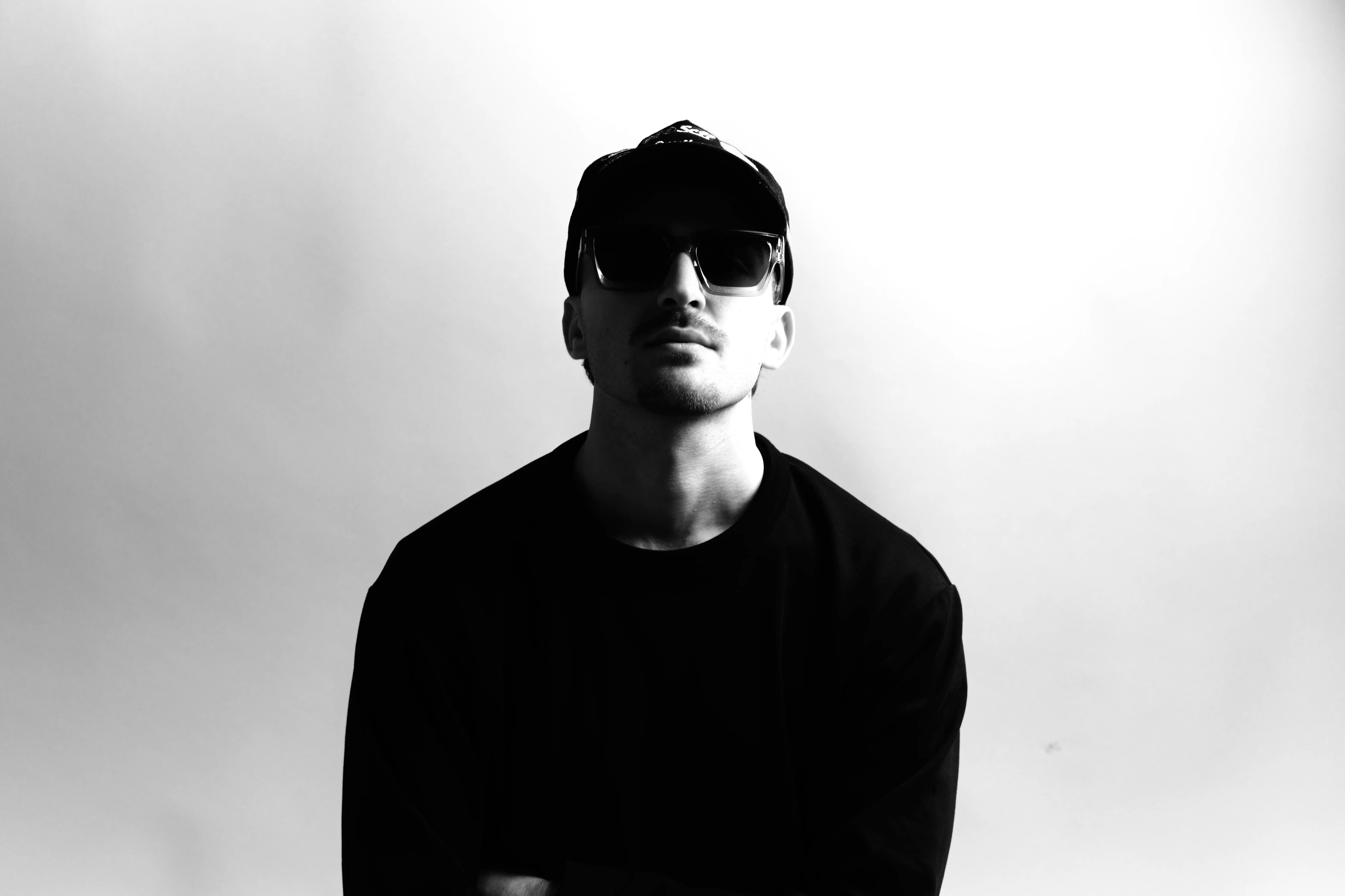 High contrast black and white portrait with sunglasses and cap looking up against bright background