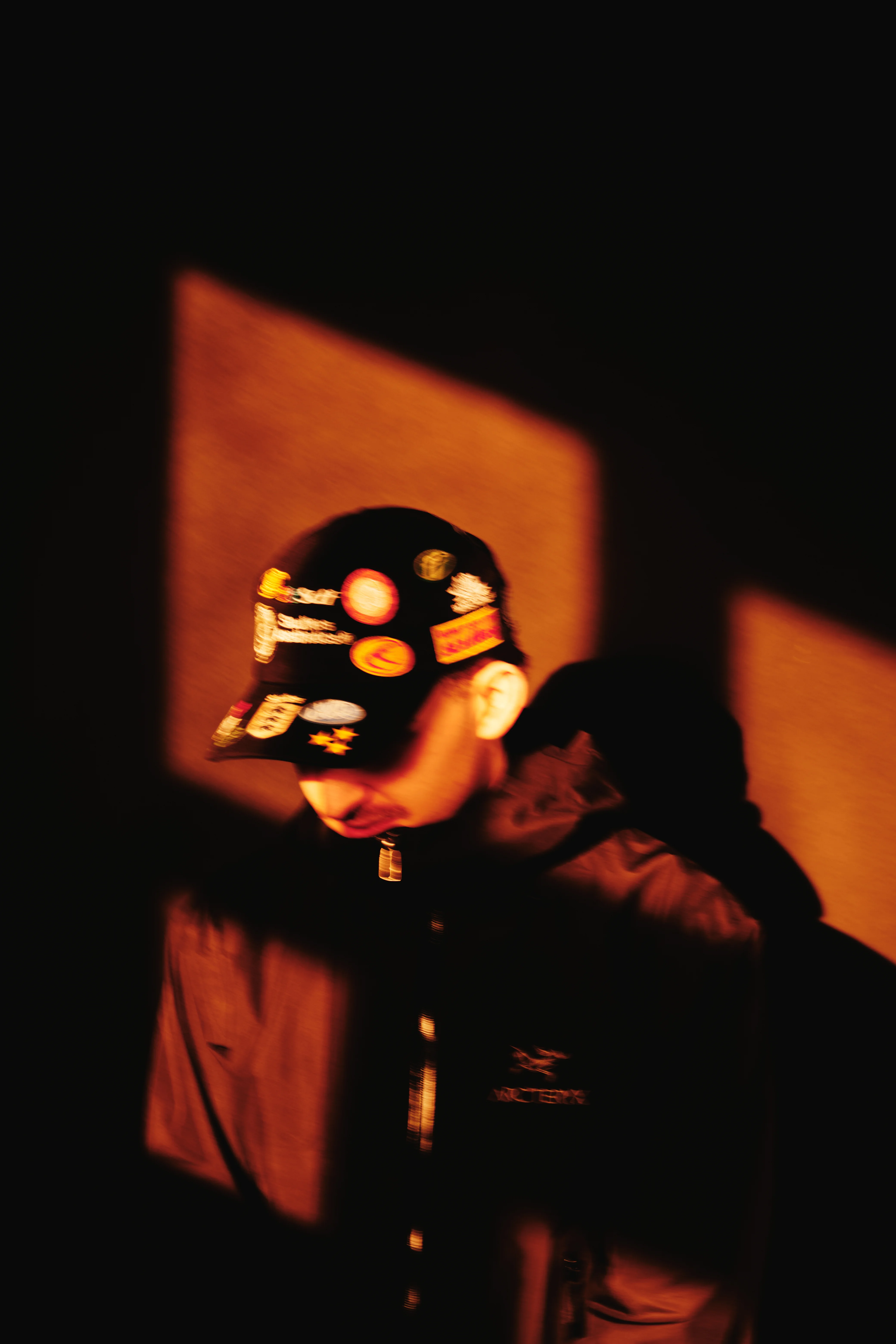Moody warm-toned portrait with sticker cap under orange ambient light