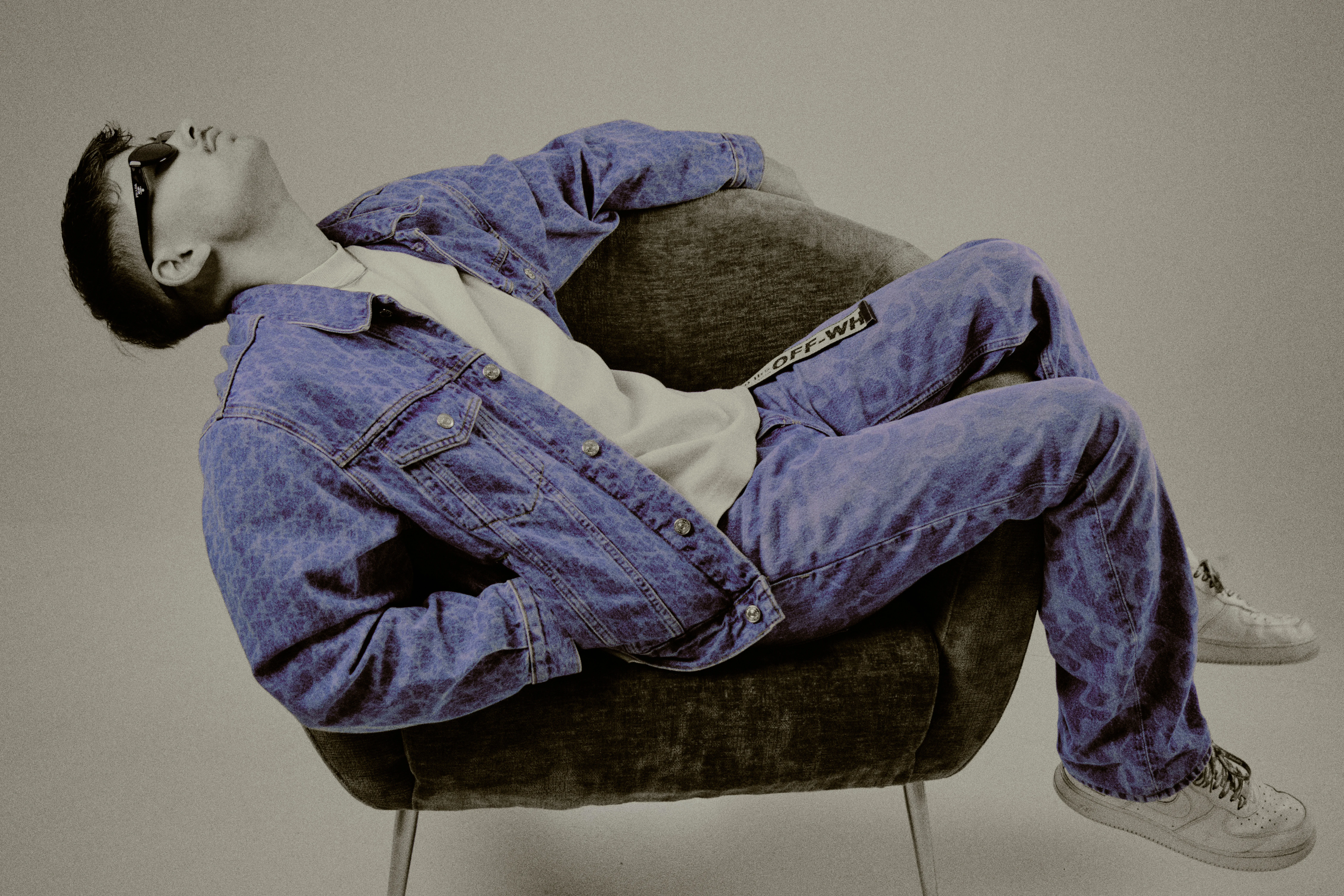 Reclining sideways in armchair wearing denim set, purple color accent with muted background