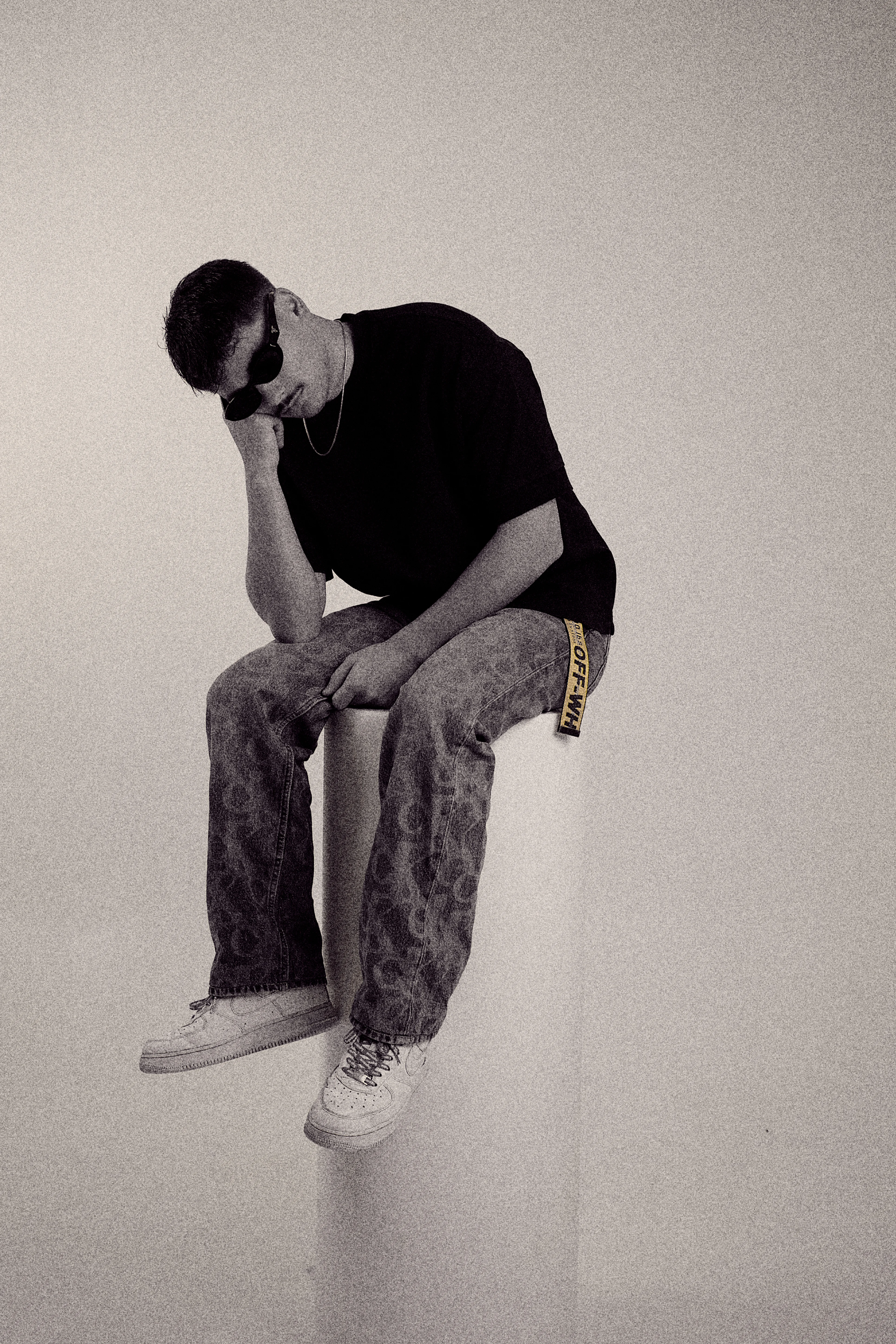 Desaturated portrait sitting on pedestal, leaning on hand in black tee and patterned pants